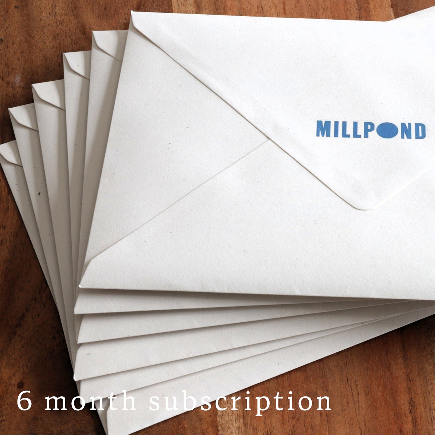Stack of white envelopes with 'MILLPOND' branding on a wooden surface, labeled as a 6 month subscription.