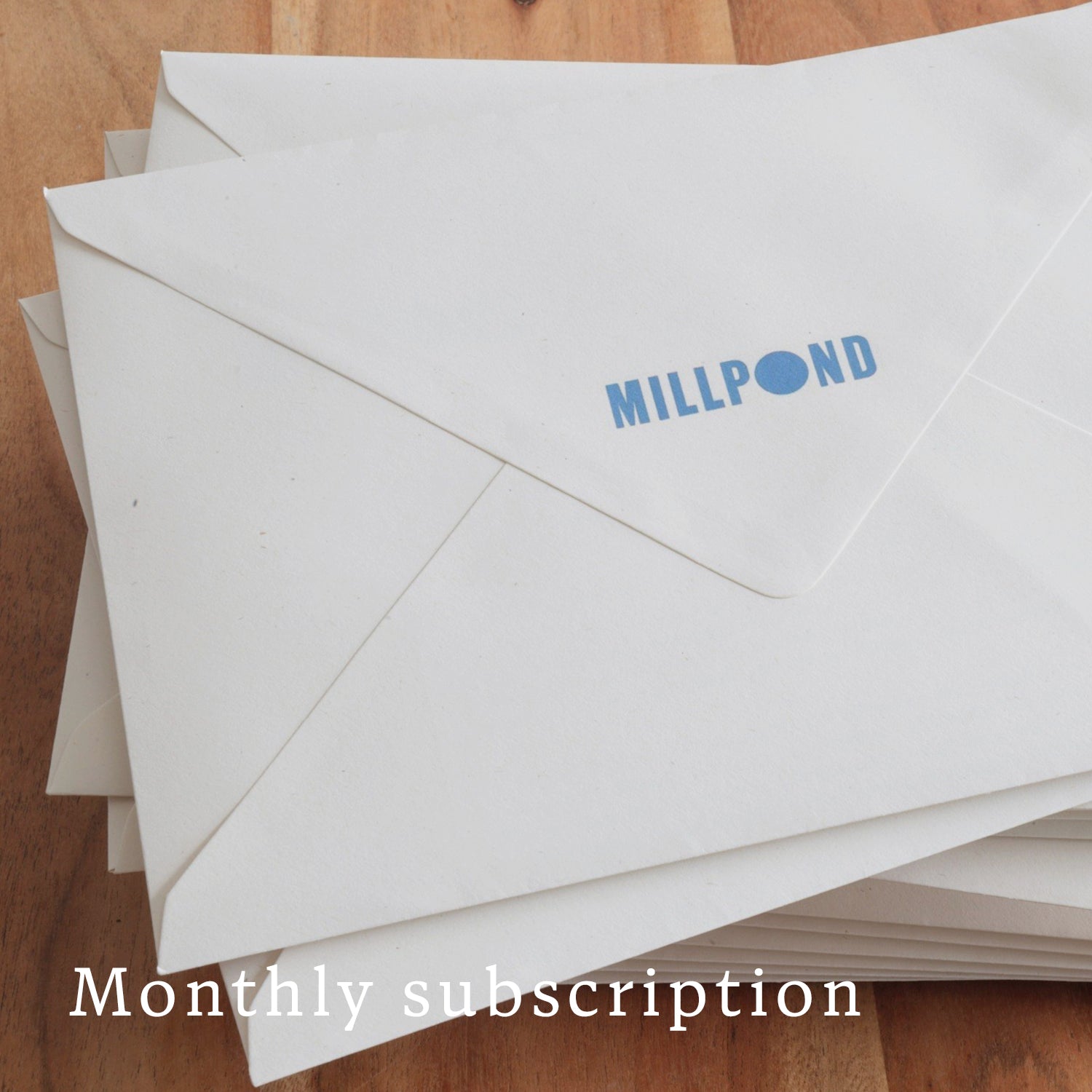 White envelopes with 'MILLPOND' branding on a wooden surface, labeled as monthly subscription.